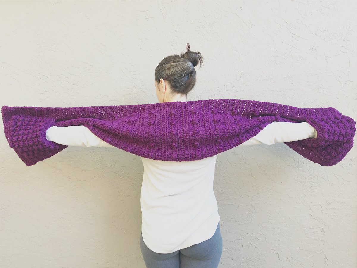 Woman with her arms held out to show pockets of crochet shawl.
