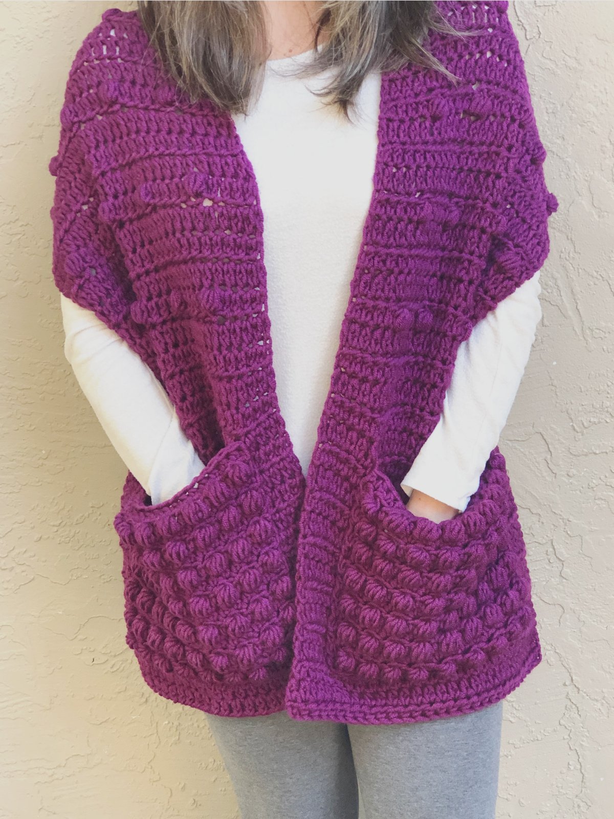 Woman with hands in pockets of purple shawl.
