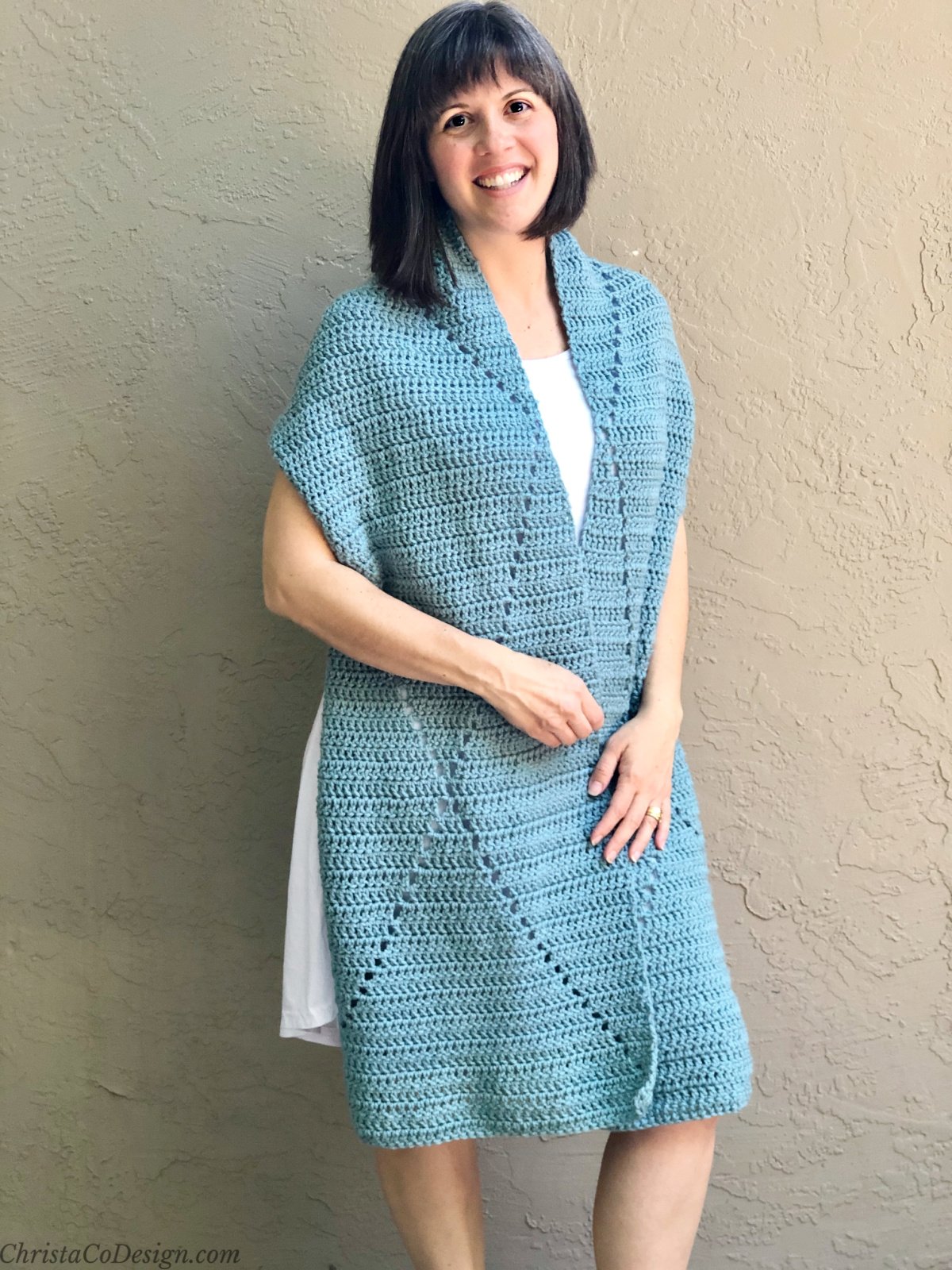 Woman smiling with blue crochet wrap draped on shoulders.