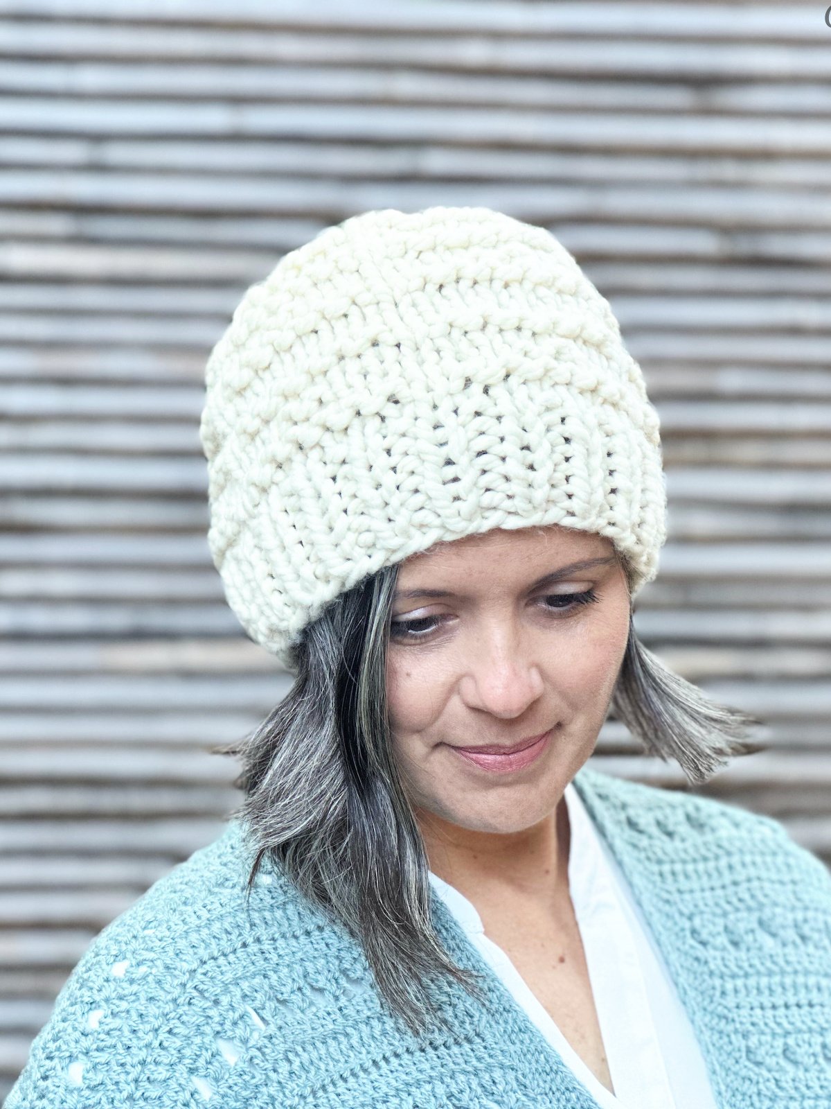 Woman smiling softly wearing chunky knit hat in off white.