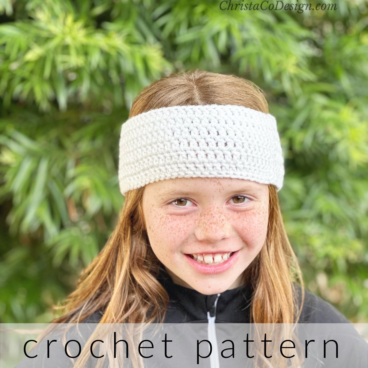 Girl with white crochet headband on smiling in front of tree.