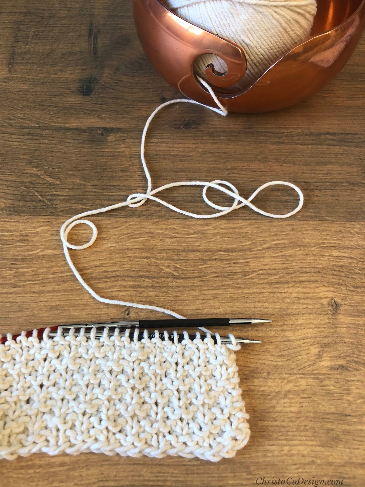 Textured fabric on knitting needles in cream yarn.