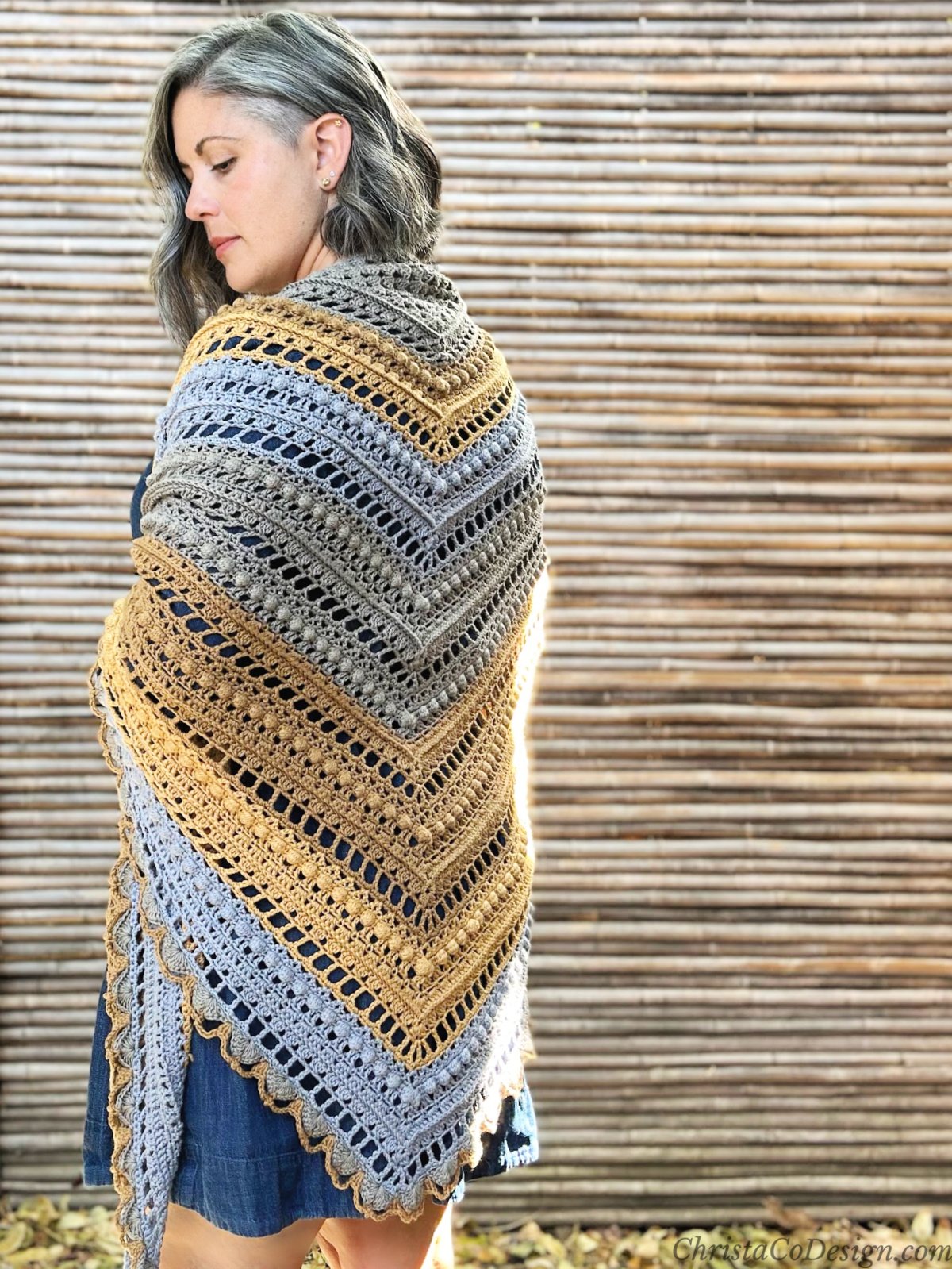 Woman wrapped in crochet shawl of textured stitches and fall colors.