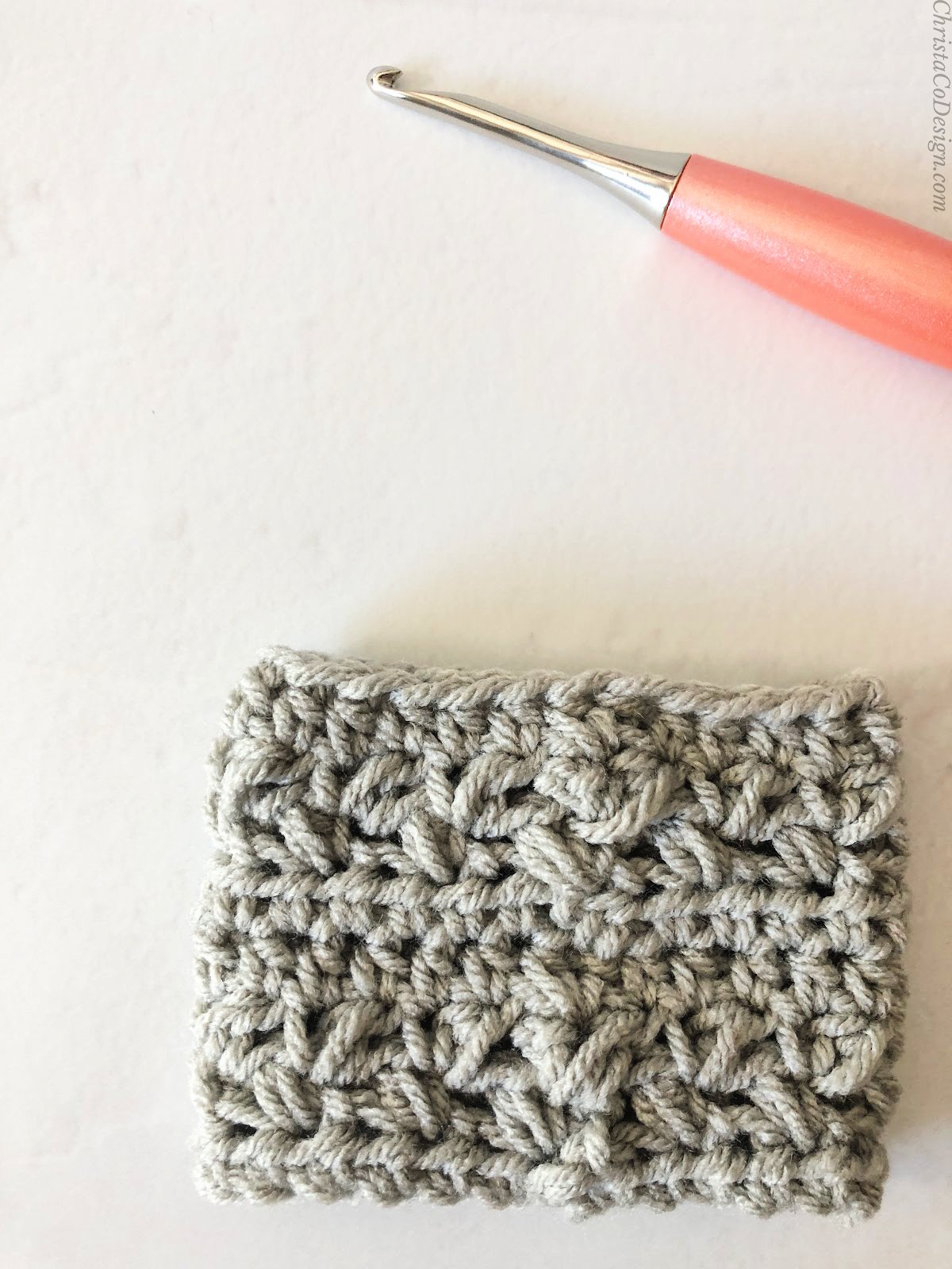 Grey mug sleeve with peach crochet hook.