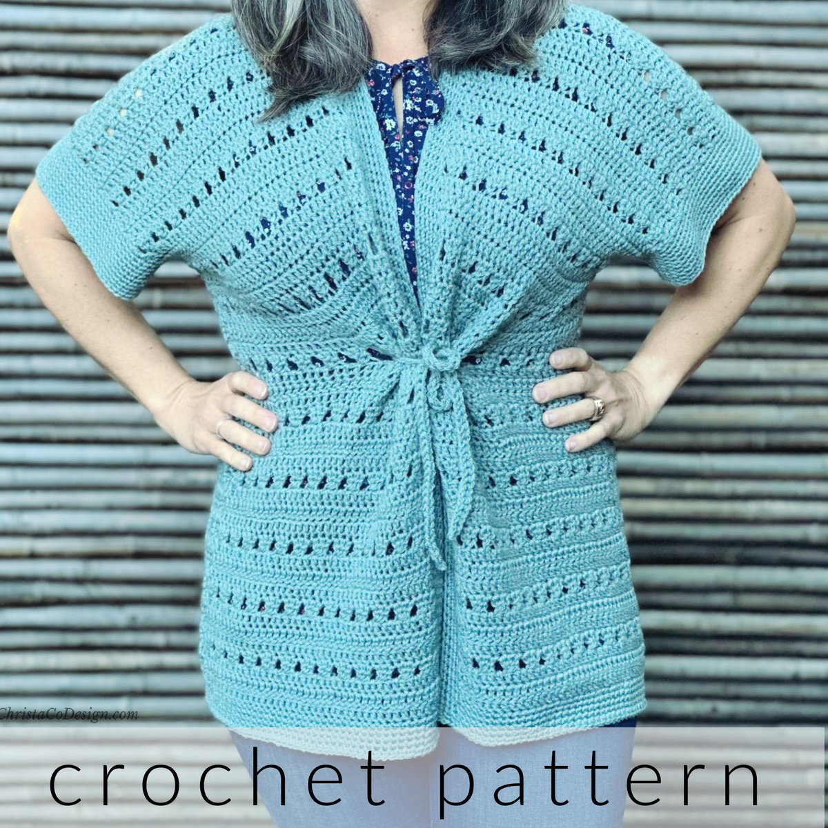 Woman with hands on hips wear crochet cardigan in sage with belted tie in front.
