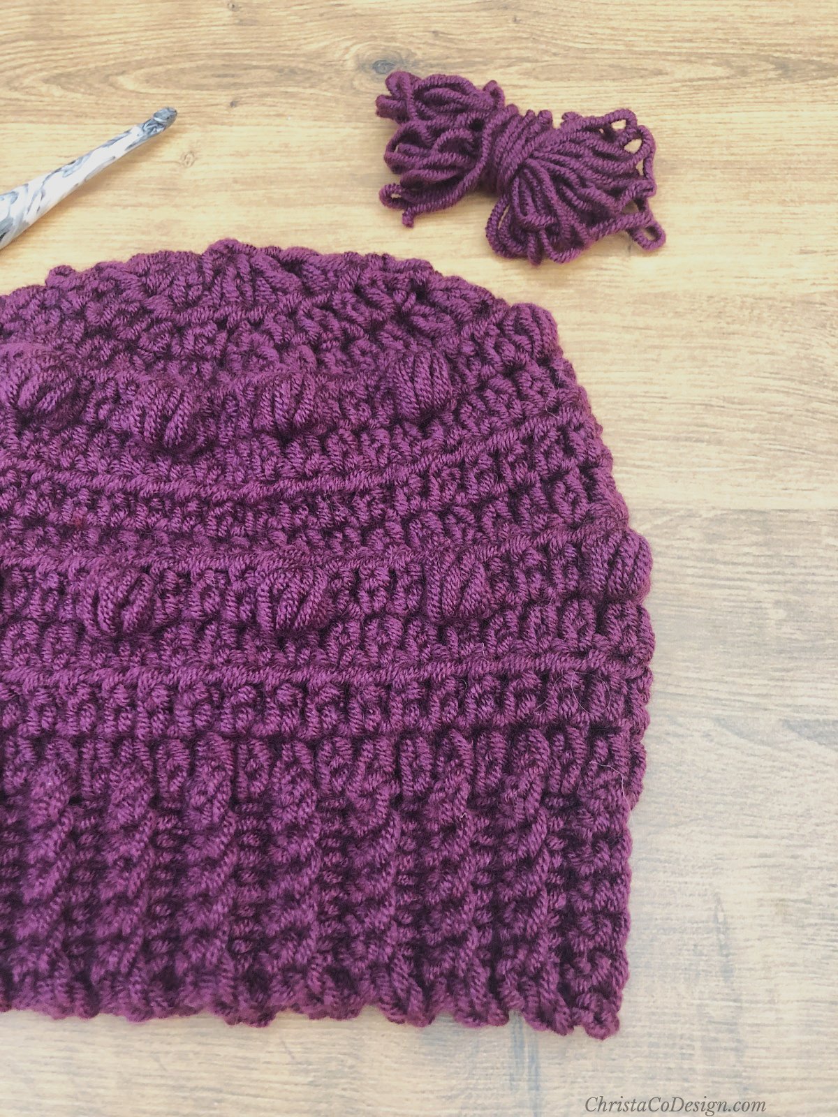 Chunky hat in purple with bobbles next to yarn.