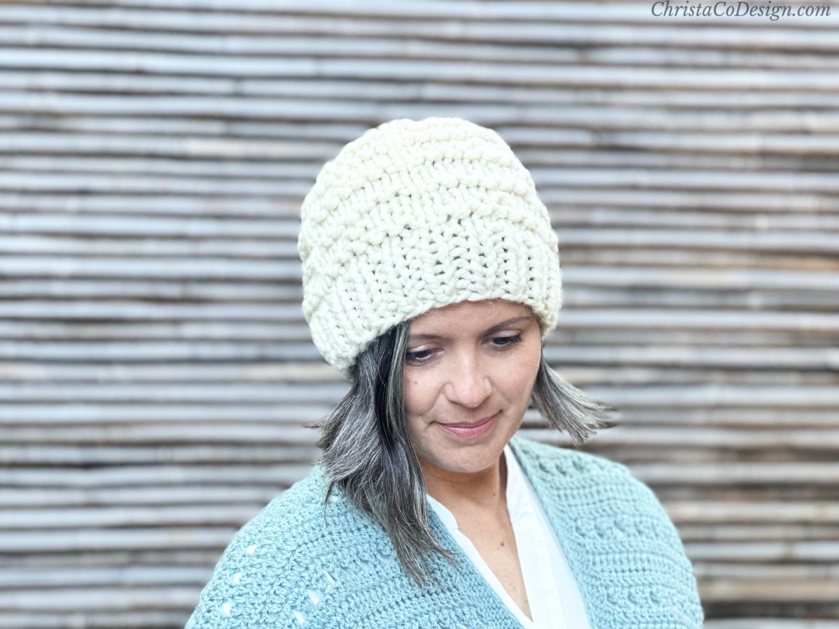 Woman lookin down in cream knit hat.