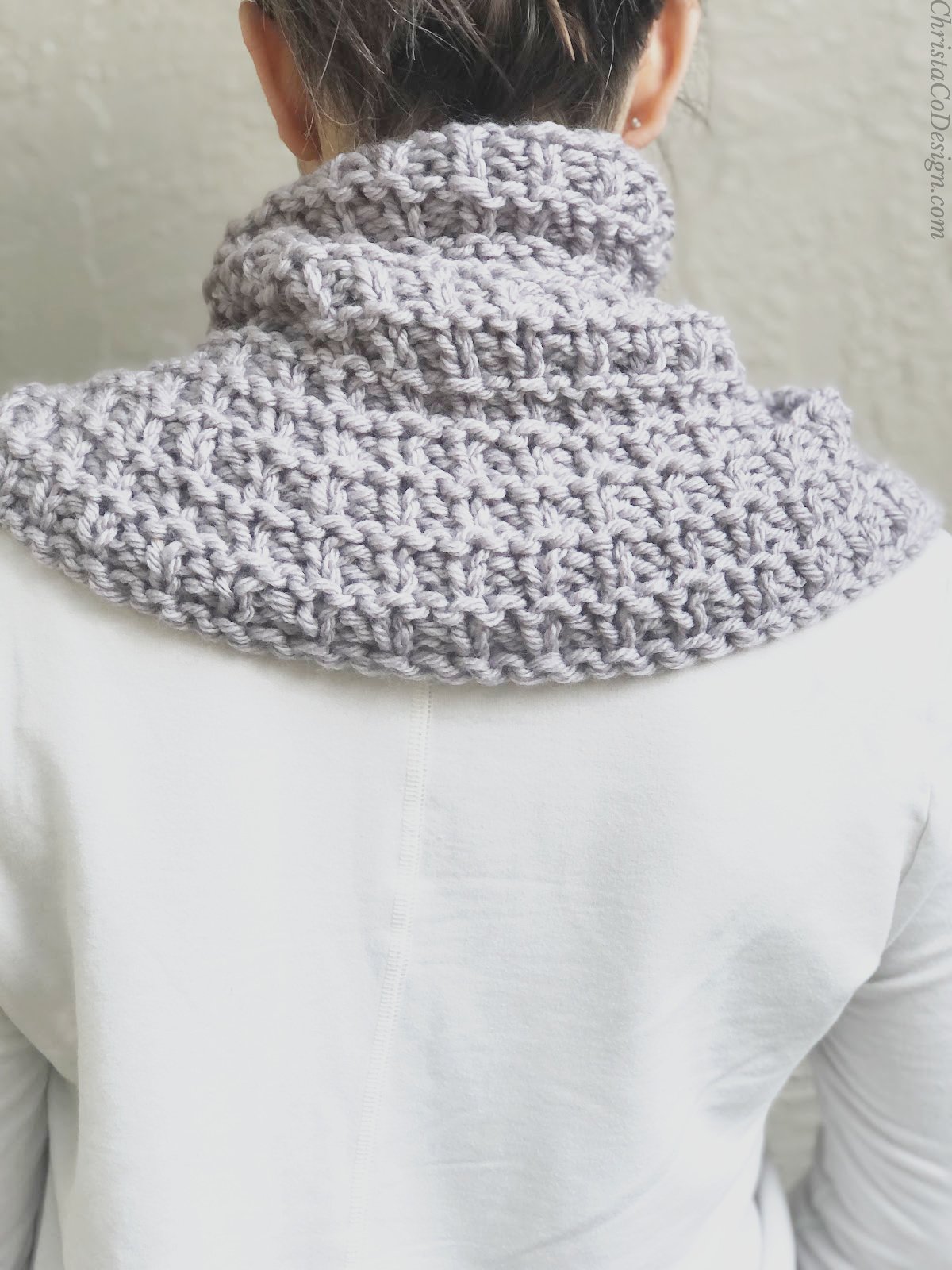 Woman turned with purple knit neck warmer on shoulders.