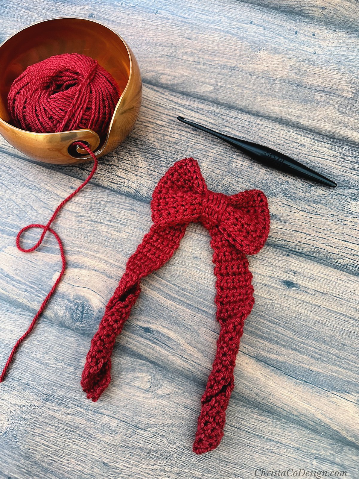 Crochet bow in red yarn next to yarn bowl and hook.