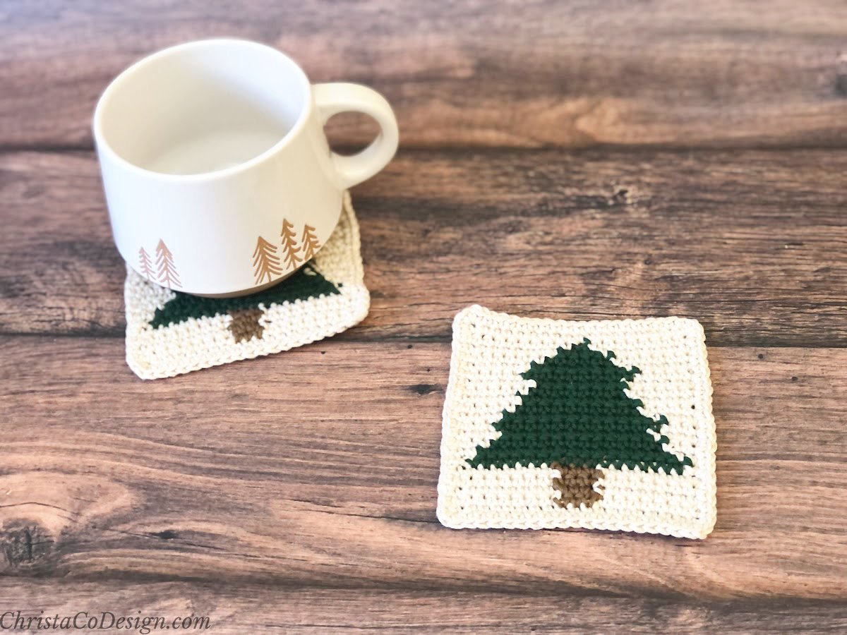 Two crochet coasters with christmas tree on them, on with a mug on it.