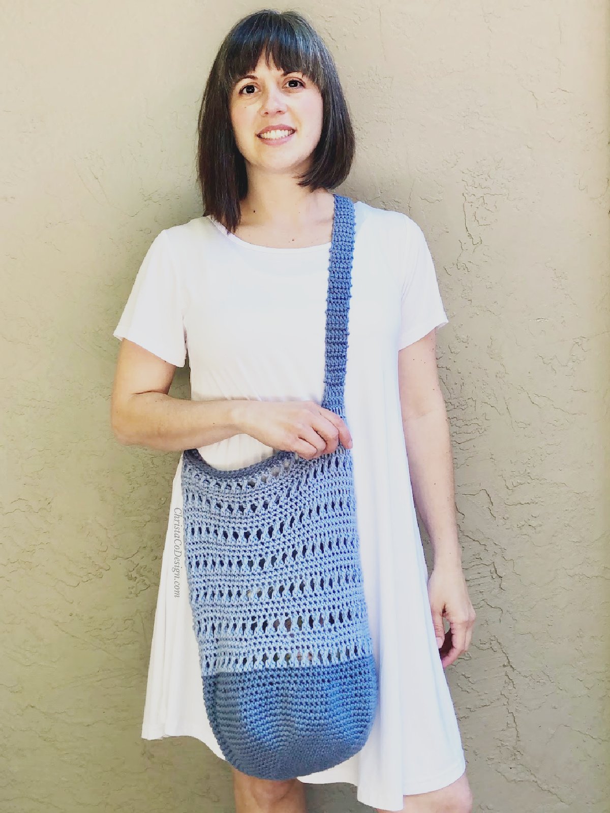 Woman in white with crochet market bag in blue across body.