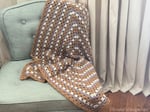 Crochet granny blanket on chair in front of curtain.
