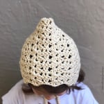 Girl wearing cream crochet bonnet with head bent.