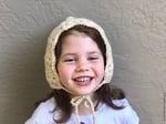 Girl smiling with crochet bonnet tied around chin.