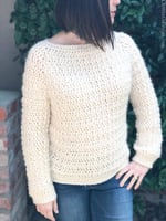 Woman with hand on hip in long sleeve creamy crochet sweater.