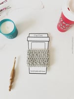 Paper cup printed with grey crochet cup sleeve, hook, candle and mug.