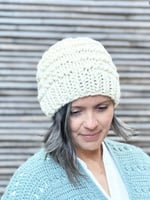 Woman smiling softly wearing chunky knit hat in off white.