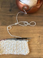Textured fabric on knitting needles in cream yarn.