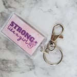 acrylic keychain with lobster hook, pink with purple text saying strong like a girl, on a marble background