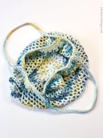 Crochet bag open with two straps on white table.