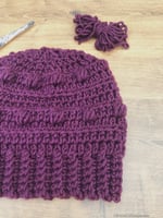 Chunky hat in purple with bobbles next to yarn.