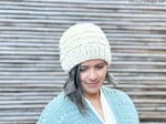 Woman lookin down in cream knit hat.