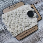 White crochet cup cozy buttoned on brown craft paper mug.