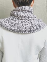 Woman turned with purple knit neck warmer on shoulders.
