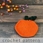 Orange crochet pumpkin coaster on table.