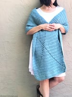 Woman wrapped in blue rectangle shawl leaning on wall.