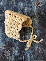 Small cream crochet pixie bonnet tied in a bow.