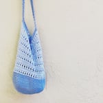 Blue crochet shoulder bag hanging in front of beige wall.