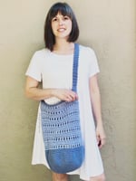 Woman in white with crochet market bag in blue across body.