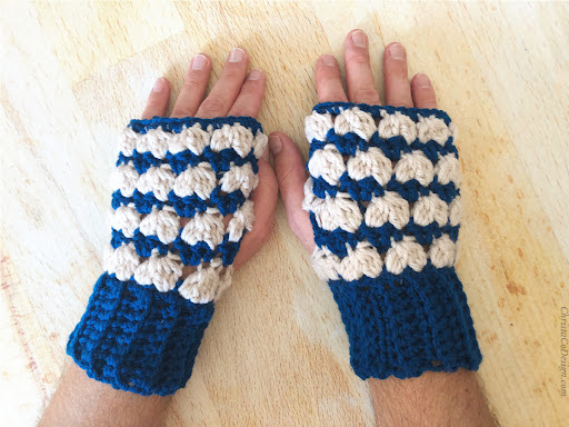 Mens hands laid flat on table in blue and cream crocheted fingerless gloves.