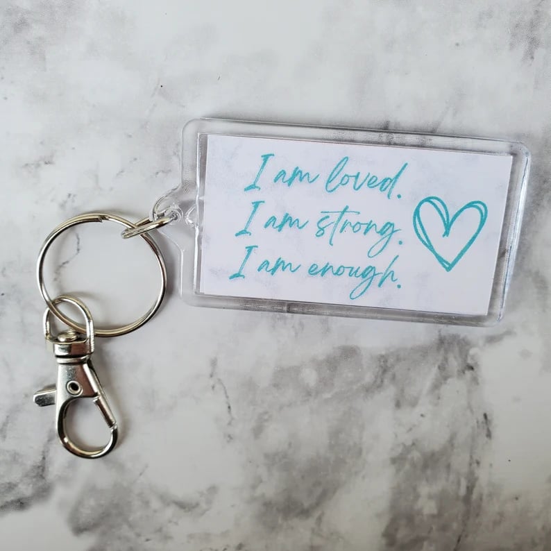 keychain with blue heart and text saying i am loved, i am strong, i am enough, all sitting on a marble surface