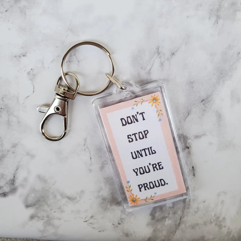 keychain with words don't stop until your proud written on a white background with a pink boarder and dried flower illustrations, all on a marble background