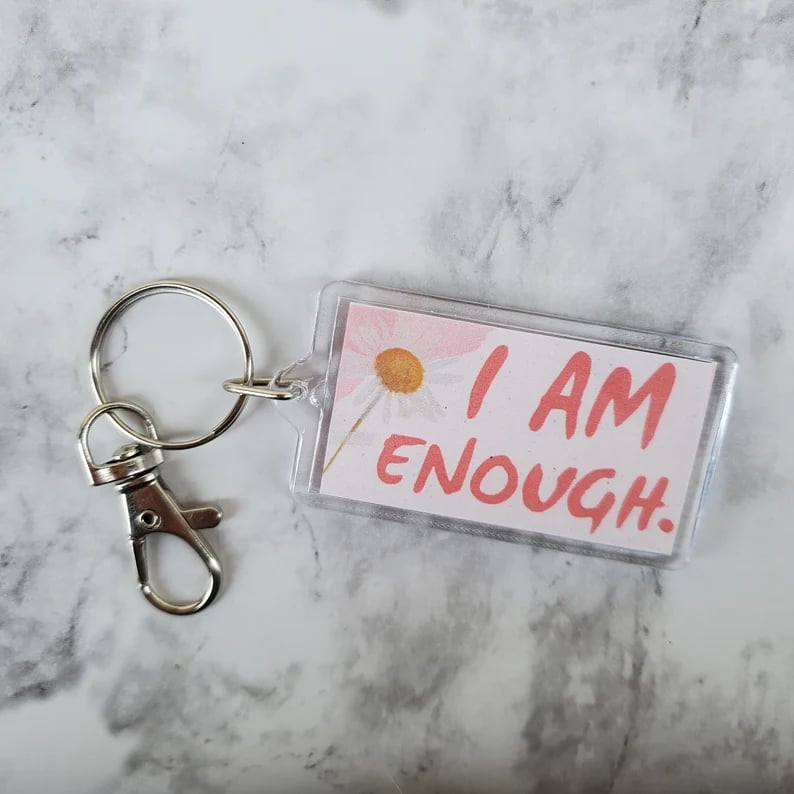 keychain with pink lettering that says I am enough with a dried flower, all sitting on a marble background